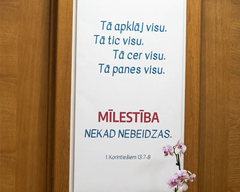 Uzraksts uz kanvas: Tā apklāj visu, 
Tā tic visu, 
Tā cer visu,
Tā panes visu. 
MĪLESTĪBA NEKAD NEBEIDZAS. 
1. Korintiešiem 13:7-8