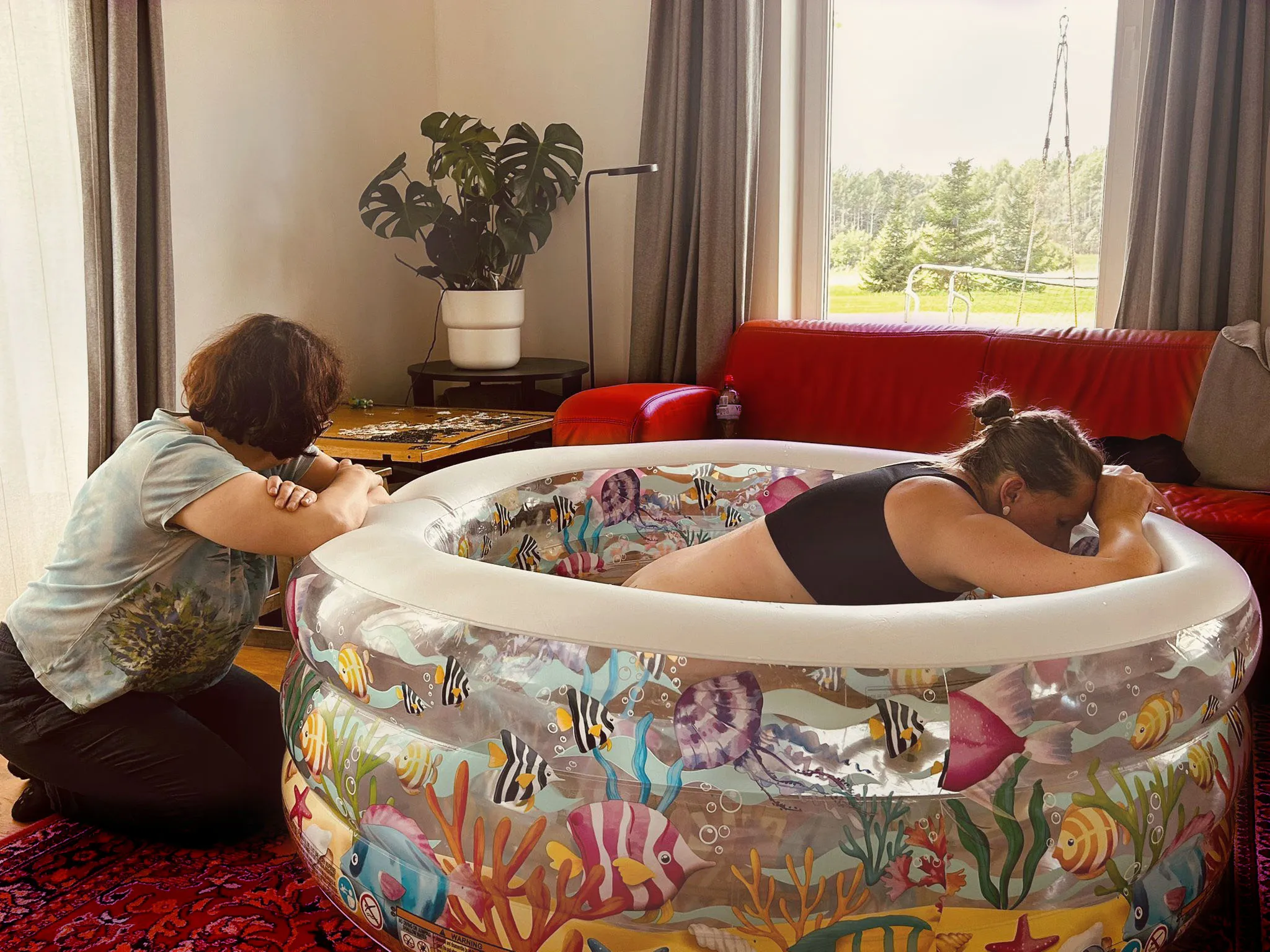 Medicīnas centra "Ģimenes sirds" vecmāte Baiba Stikute pieņem mājdzemdības kādās mājās, sieviete pieliekusies pie baseina malas pārelpo dzemdību viļņus, vecmāte blakus pie baseina